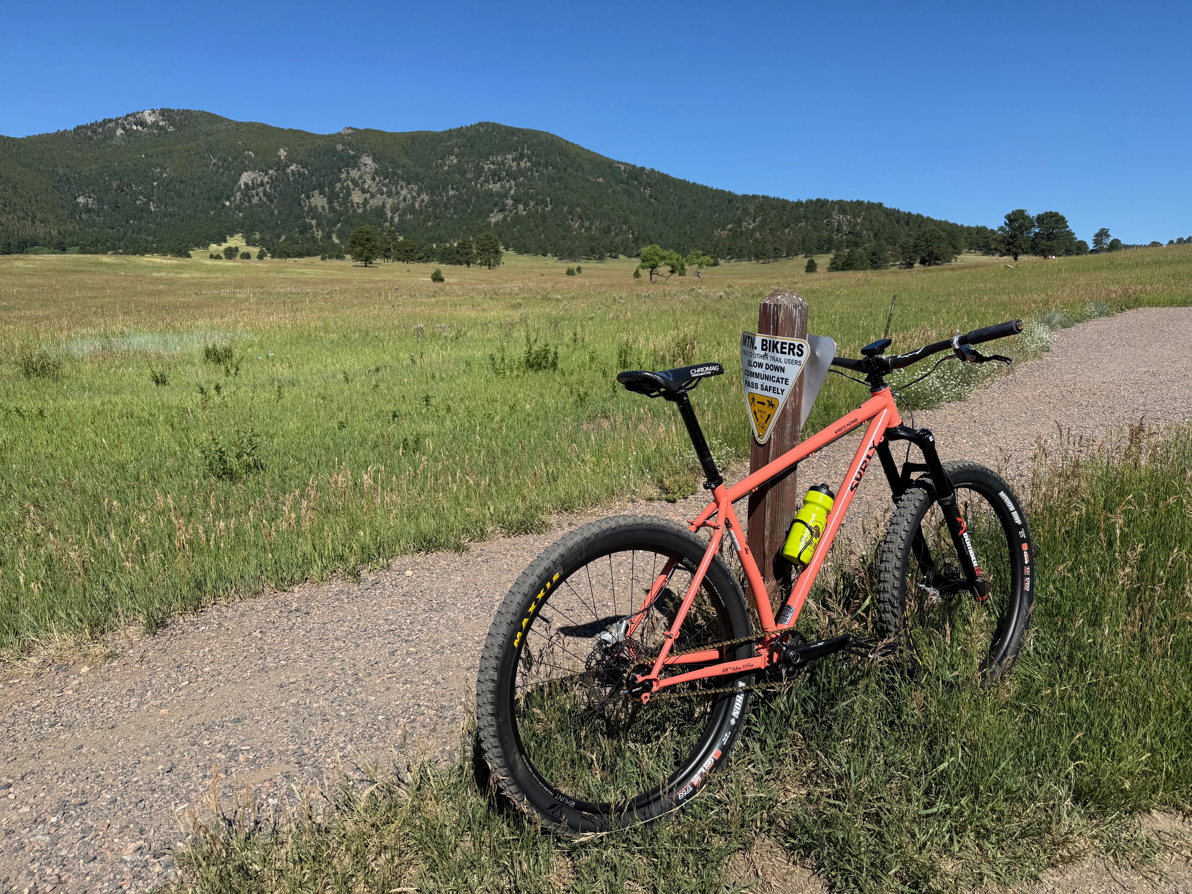 Orange Surly Karate Monkey leaning against a trail sign post in a mountain meadow
