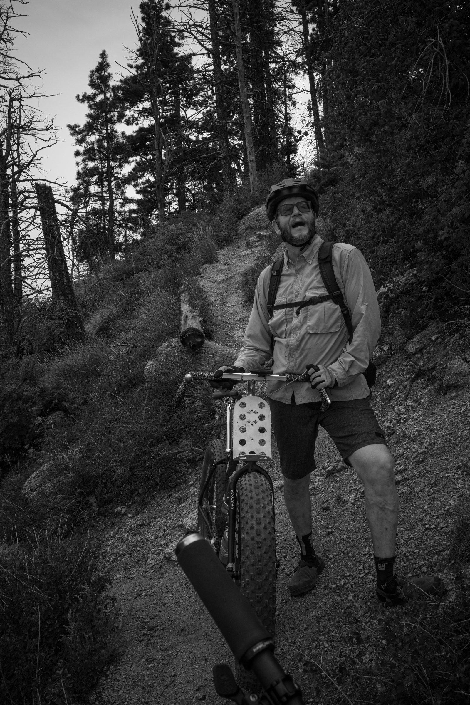 Black and white photo of a rider gassed and laughing over the bars on a steep pitch