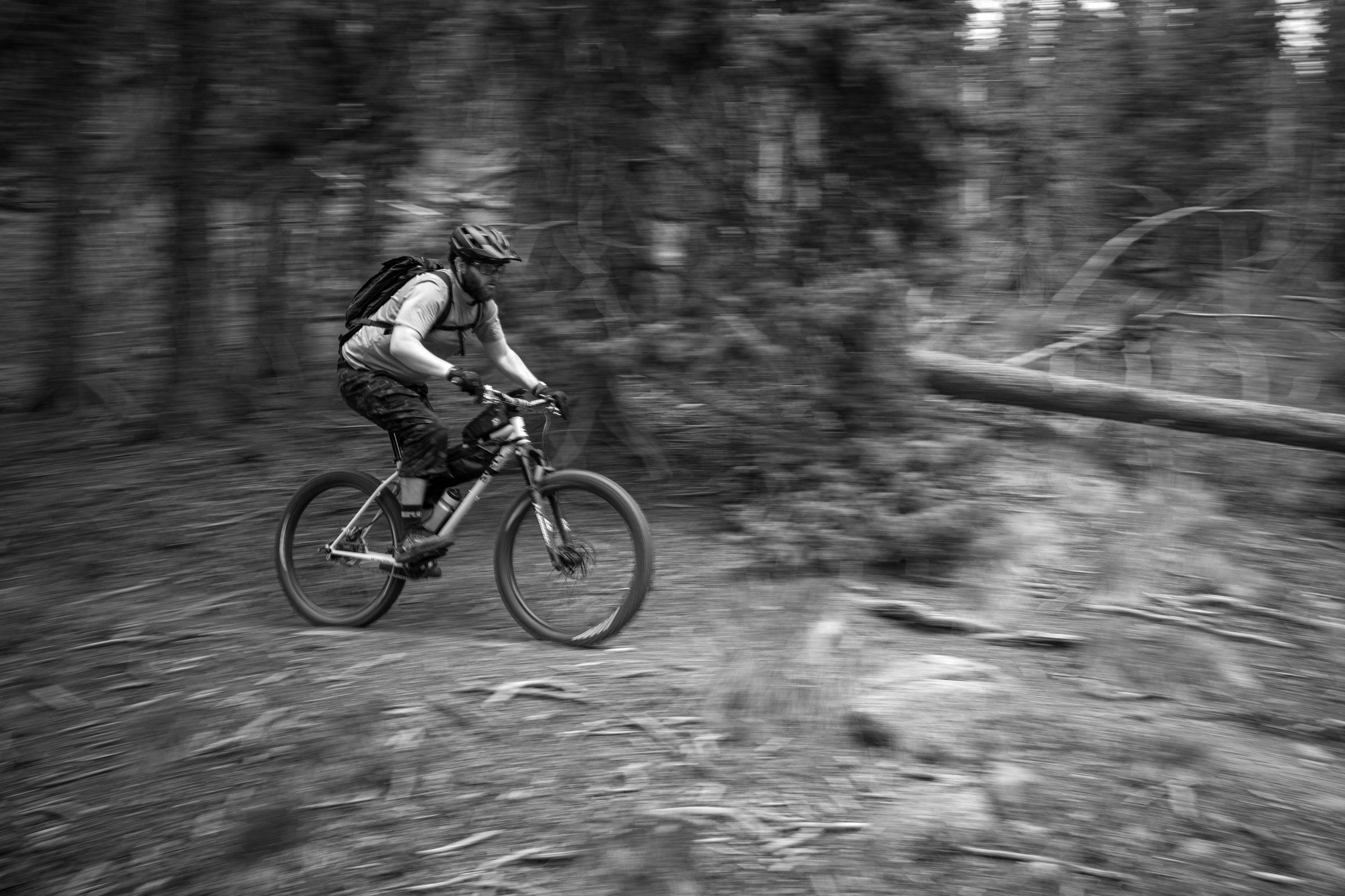 Black and white motion-pan photo of a geared rider blurring past at speed on the trail