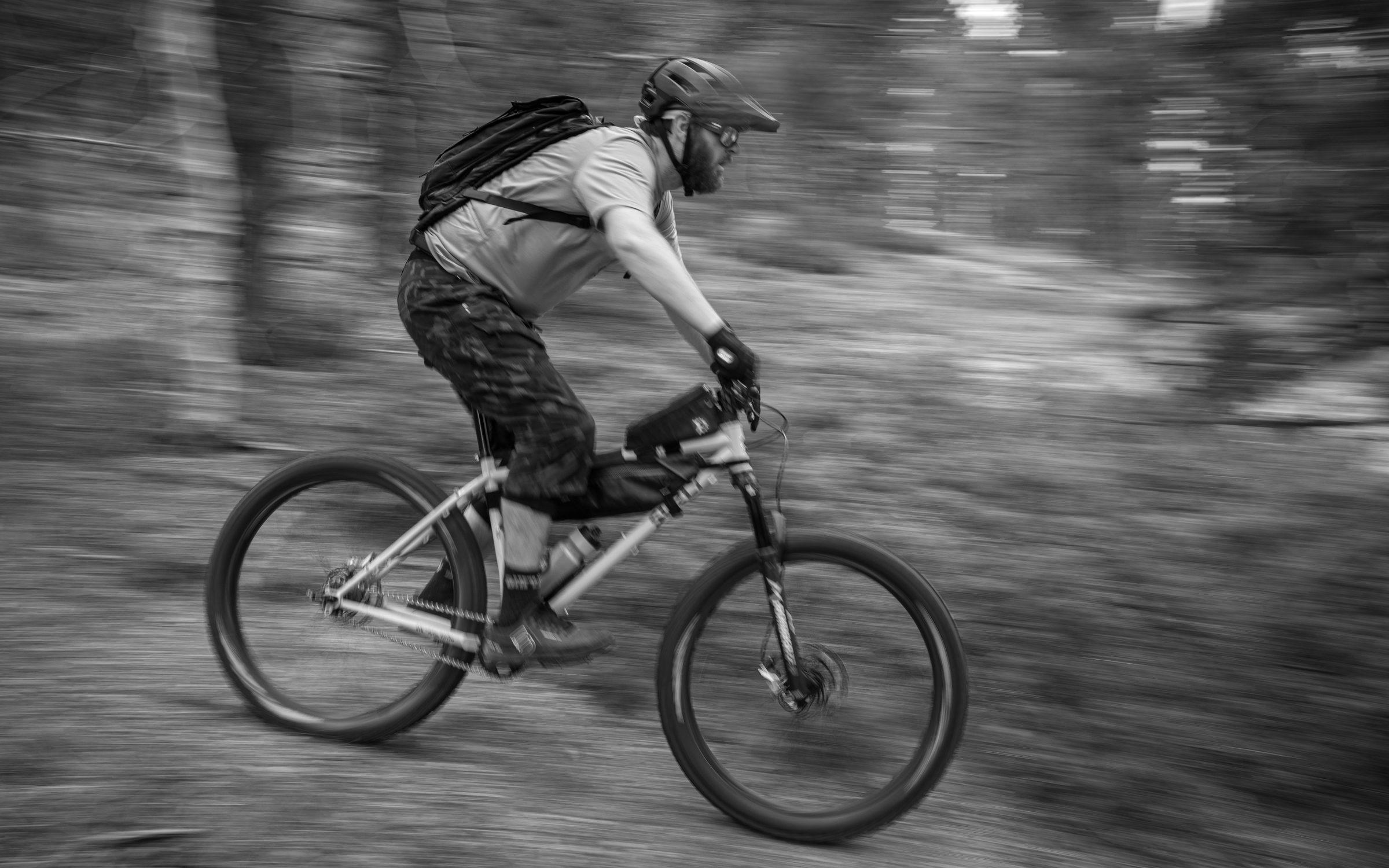 Black and white motion-pan photo of a rigid single-speed rider blurring past at speed