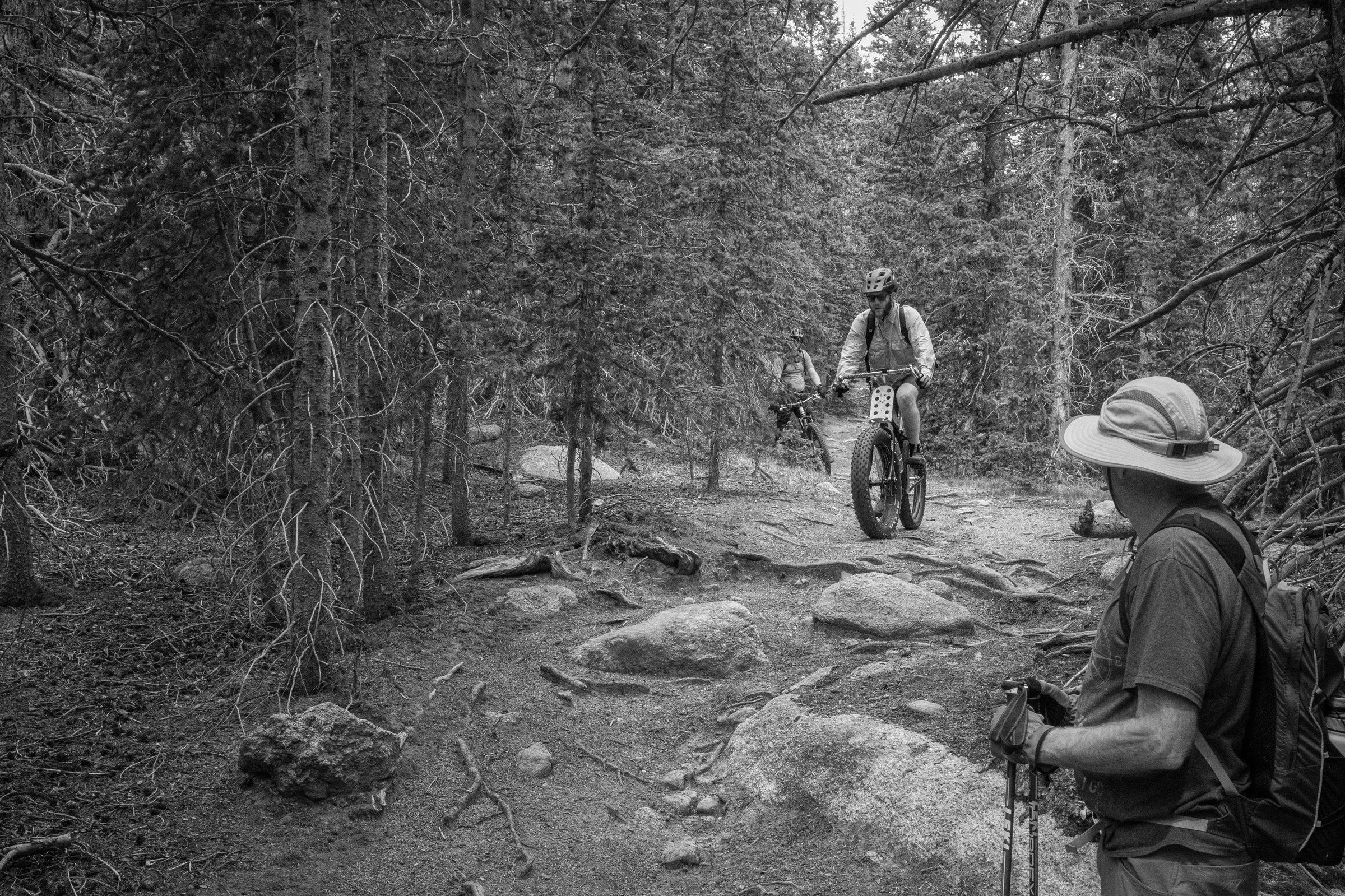 Black and white photo of three riders and a hiker gathered on a trail in dense woods