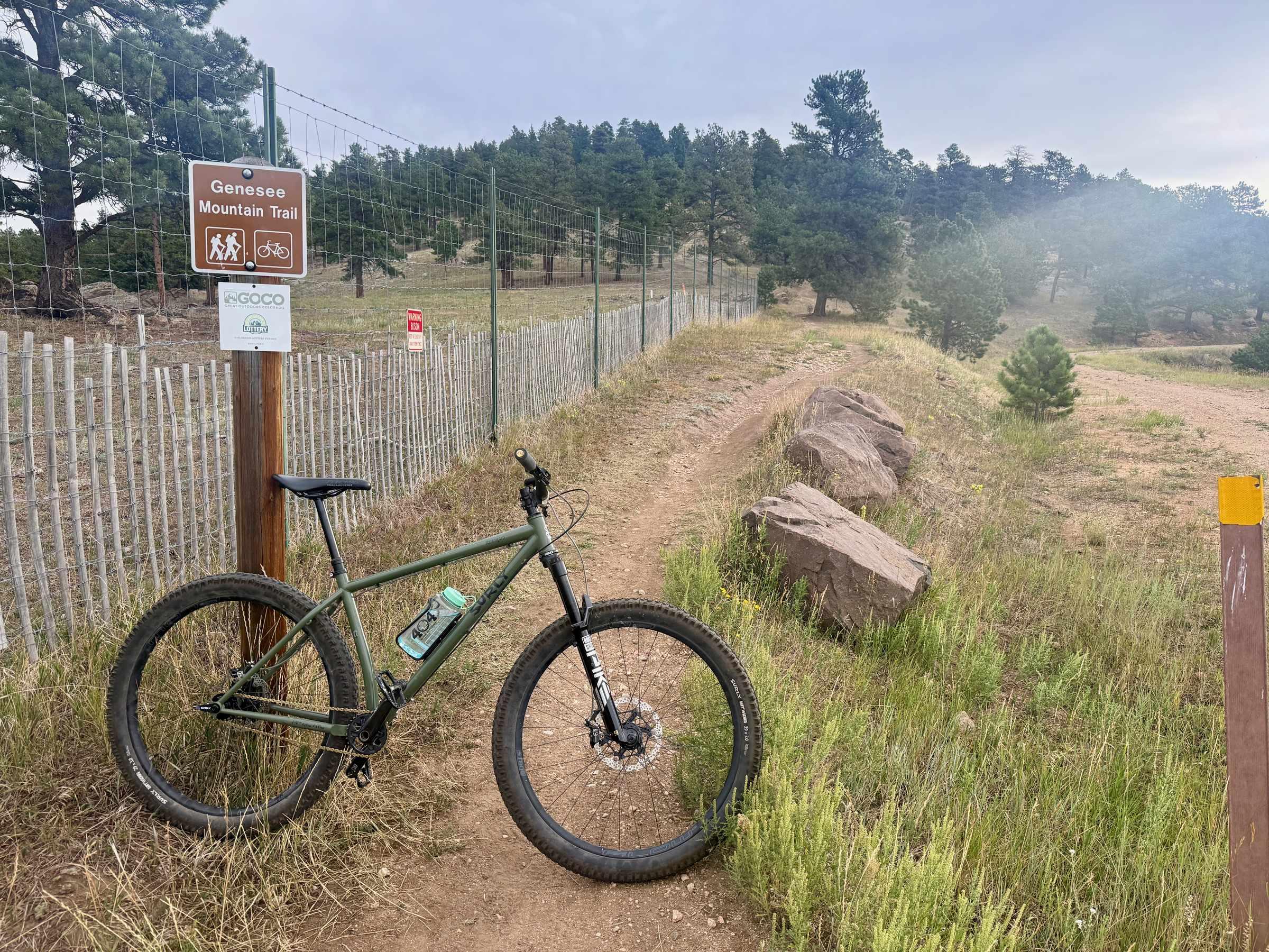 Single-speed mountain bike leaning against the Genesee Mountain Trail sign at the singletrack entrance