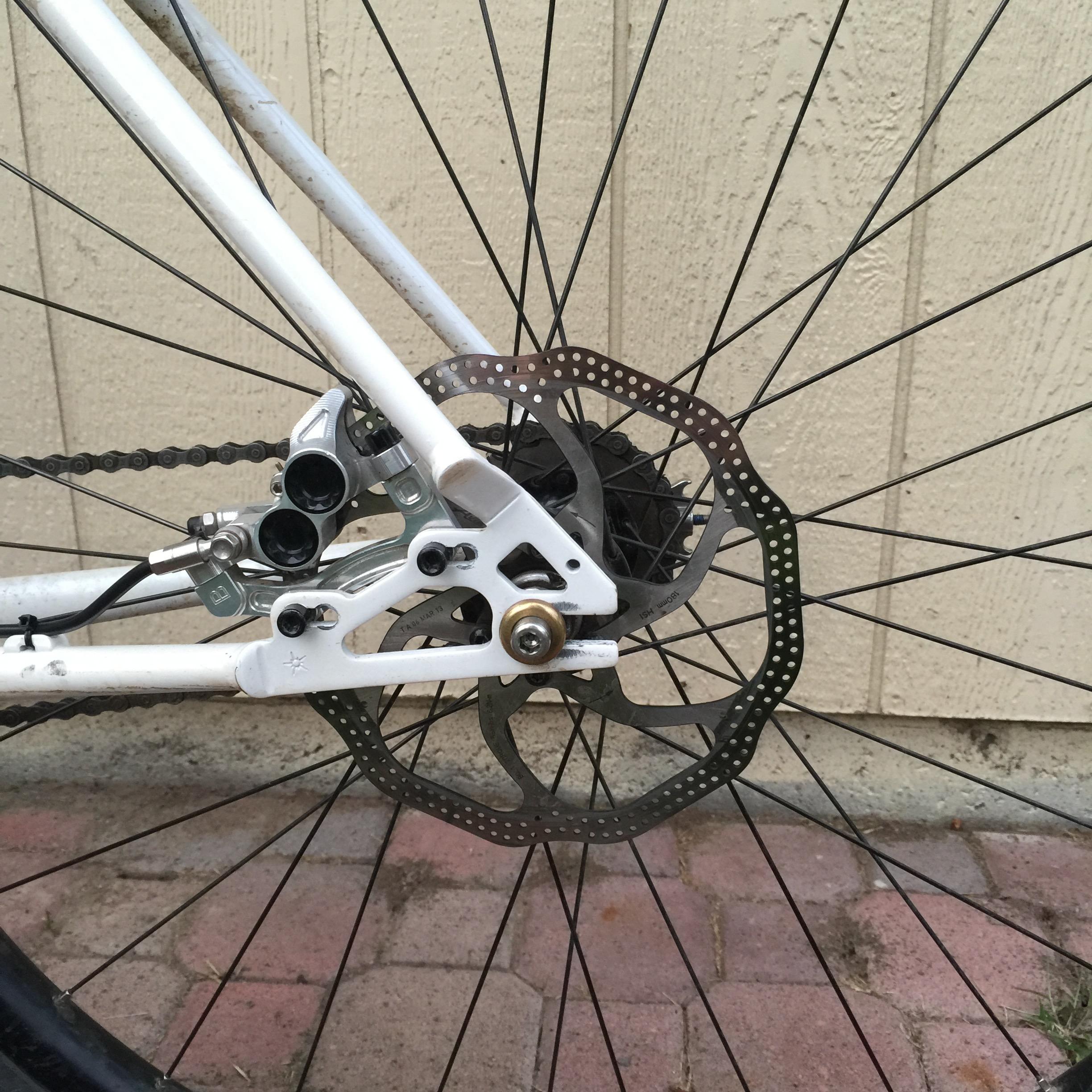 Close-up of the Inbred's rear disc brake, cassette, and hub against a wall