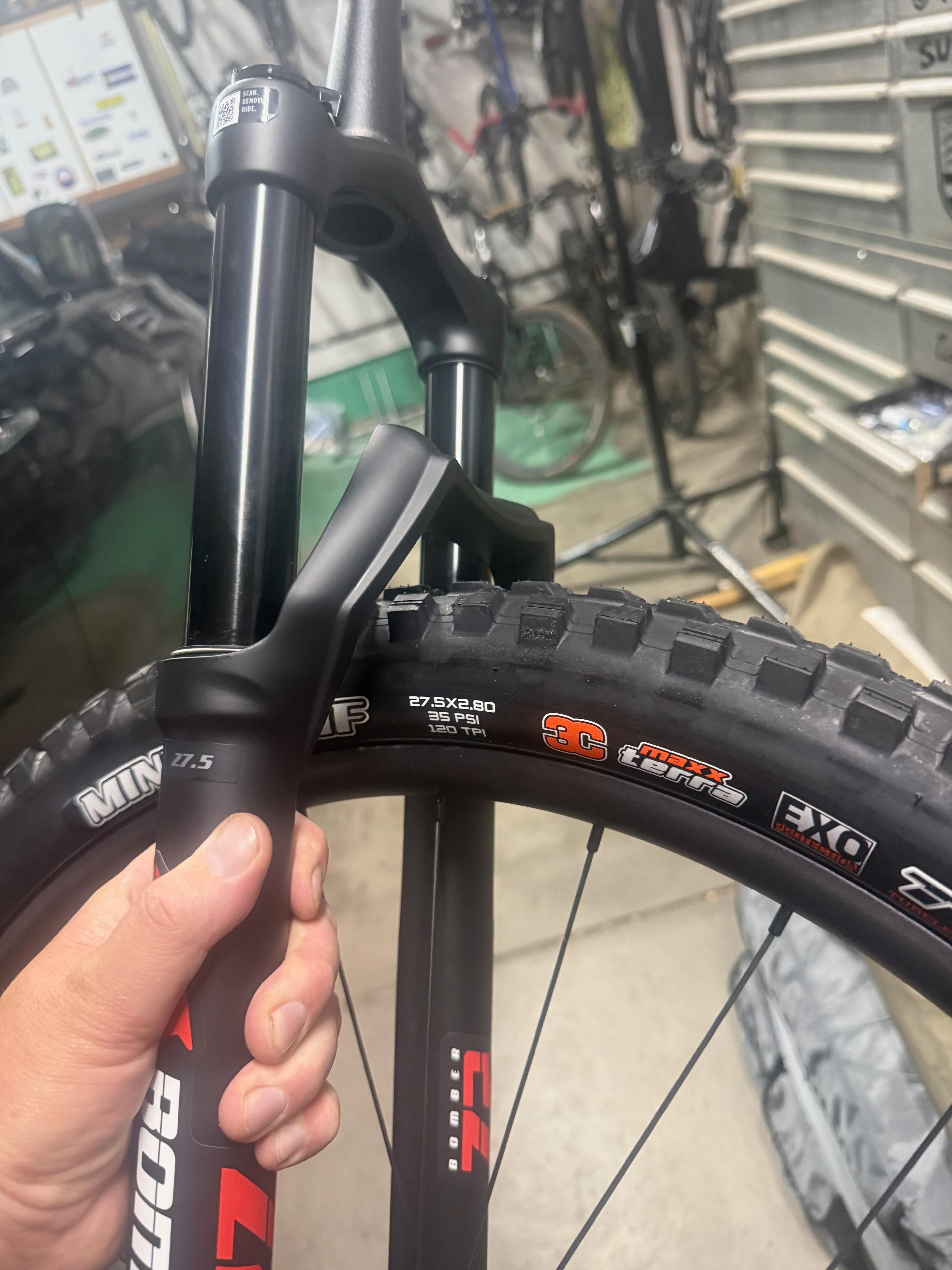 Hand holding the Marzocchi Bomber Z2 E-Opt fork next to the mounted 27.5x2.80 rear tire, checking clearance