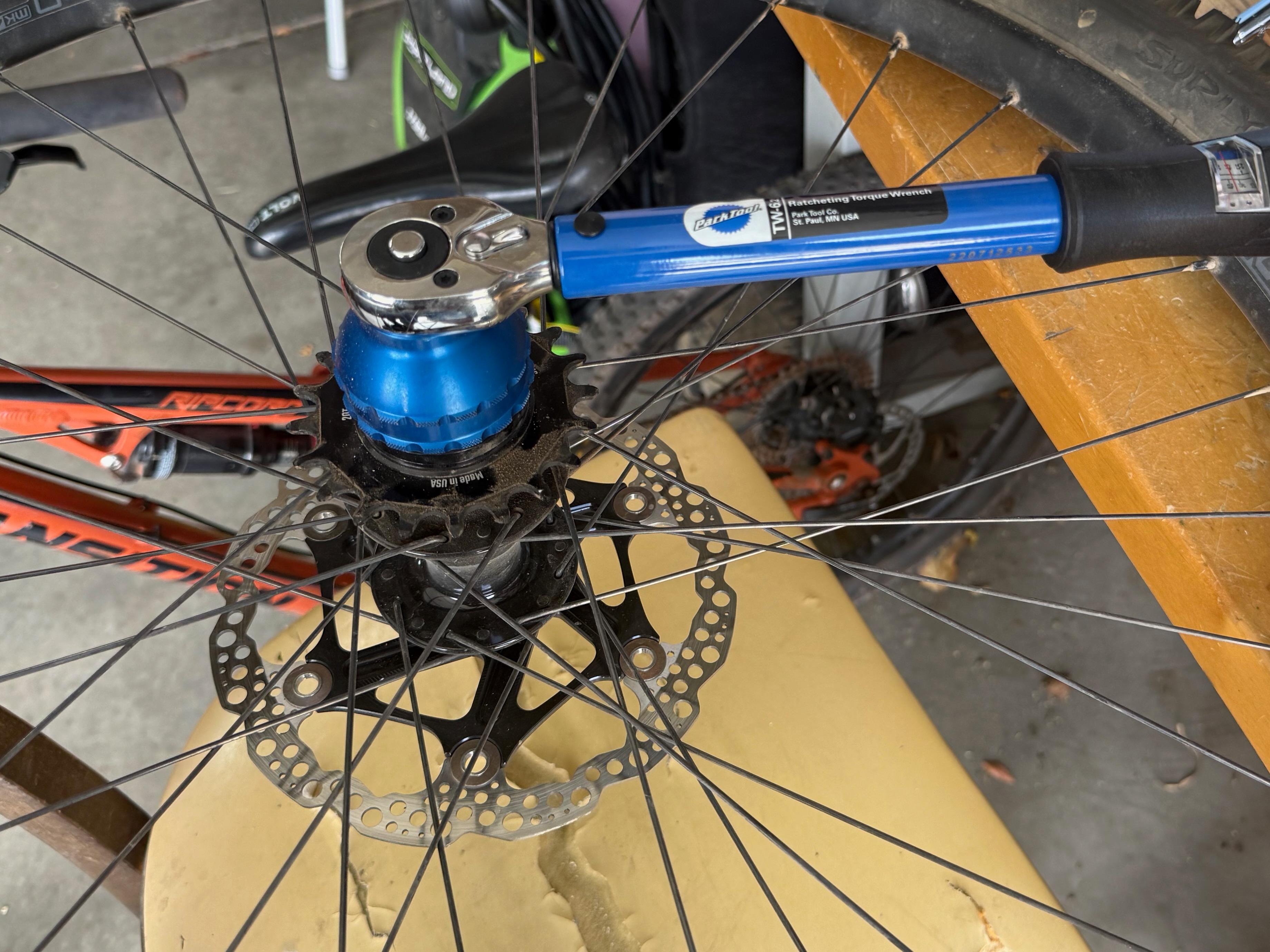 Close-up of a rear disc brake rotor and cassette on a bike wheel, with a torque wrench tightening the hub