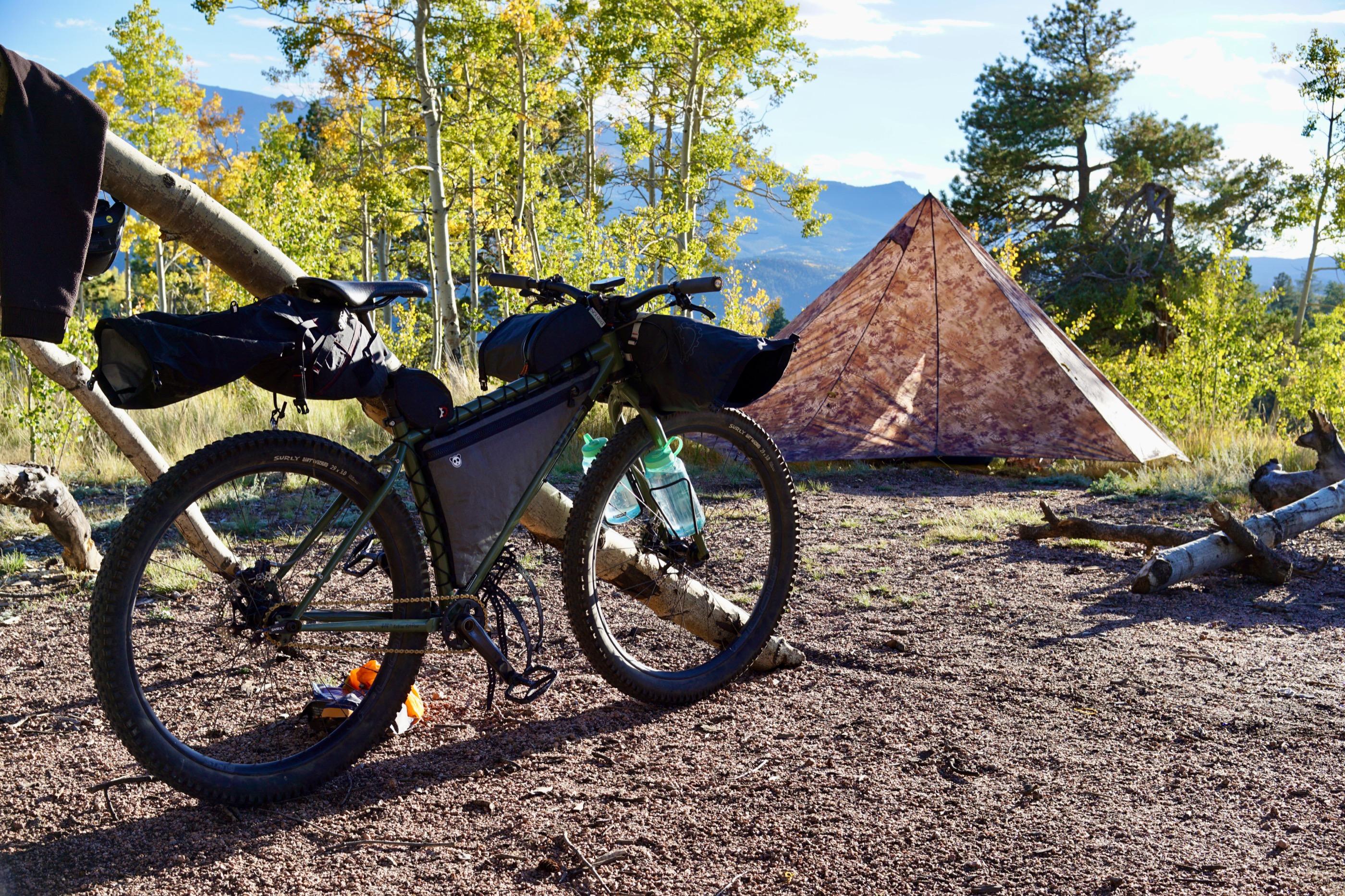 A pyramid-style bikepacking tent pitched in a clearing of turning aspens with Pikes Peak visible on the horizon