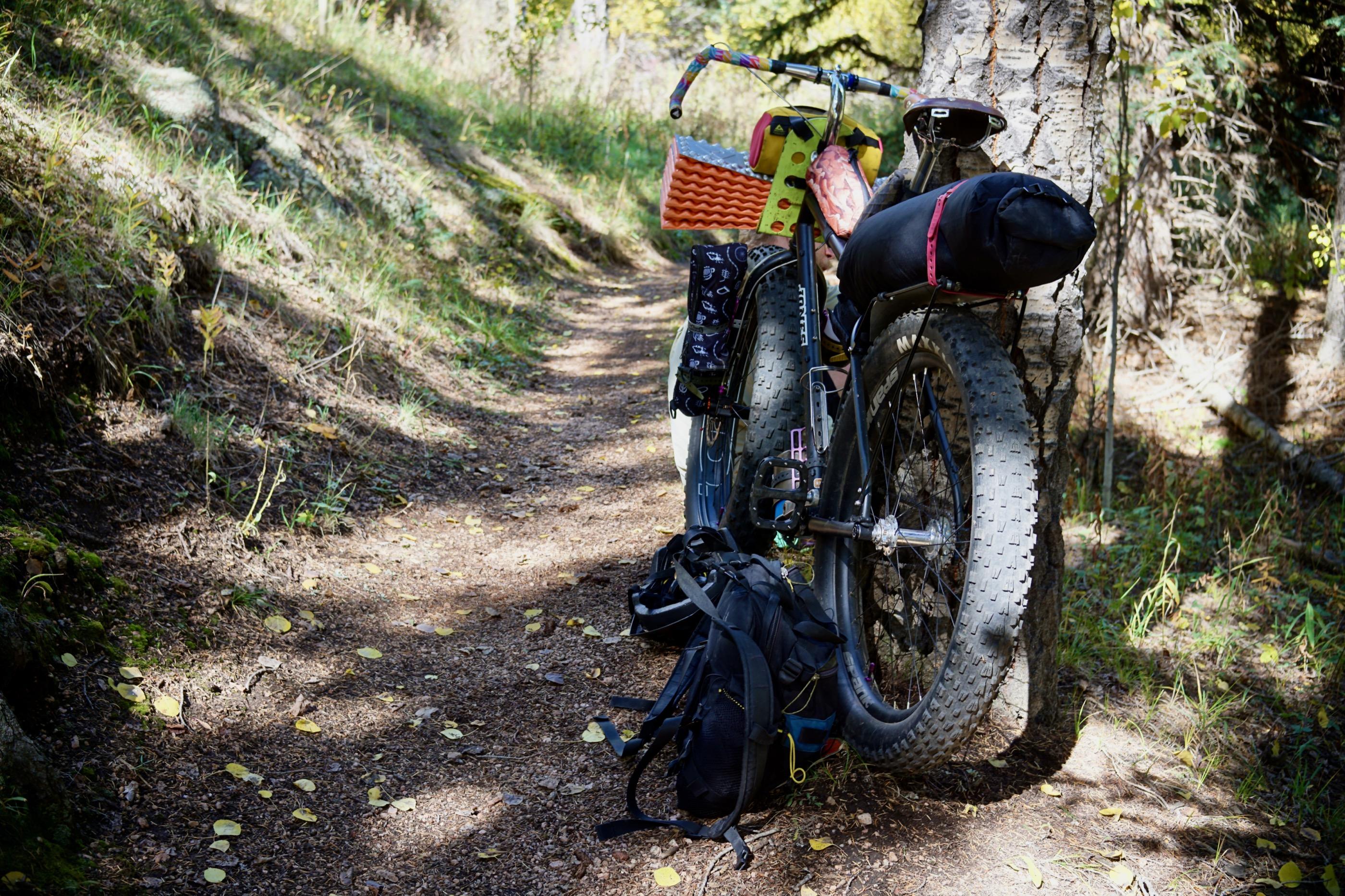 A loaded bikepacking setup on singletrack showing a colorful handlebar roll, sleeping pad, and frame bag in close detail