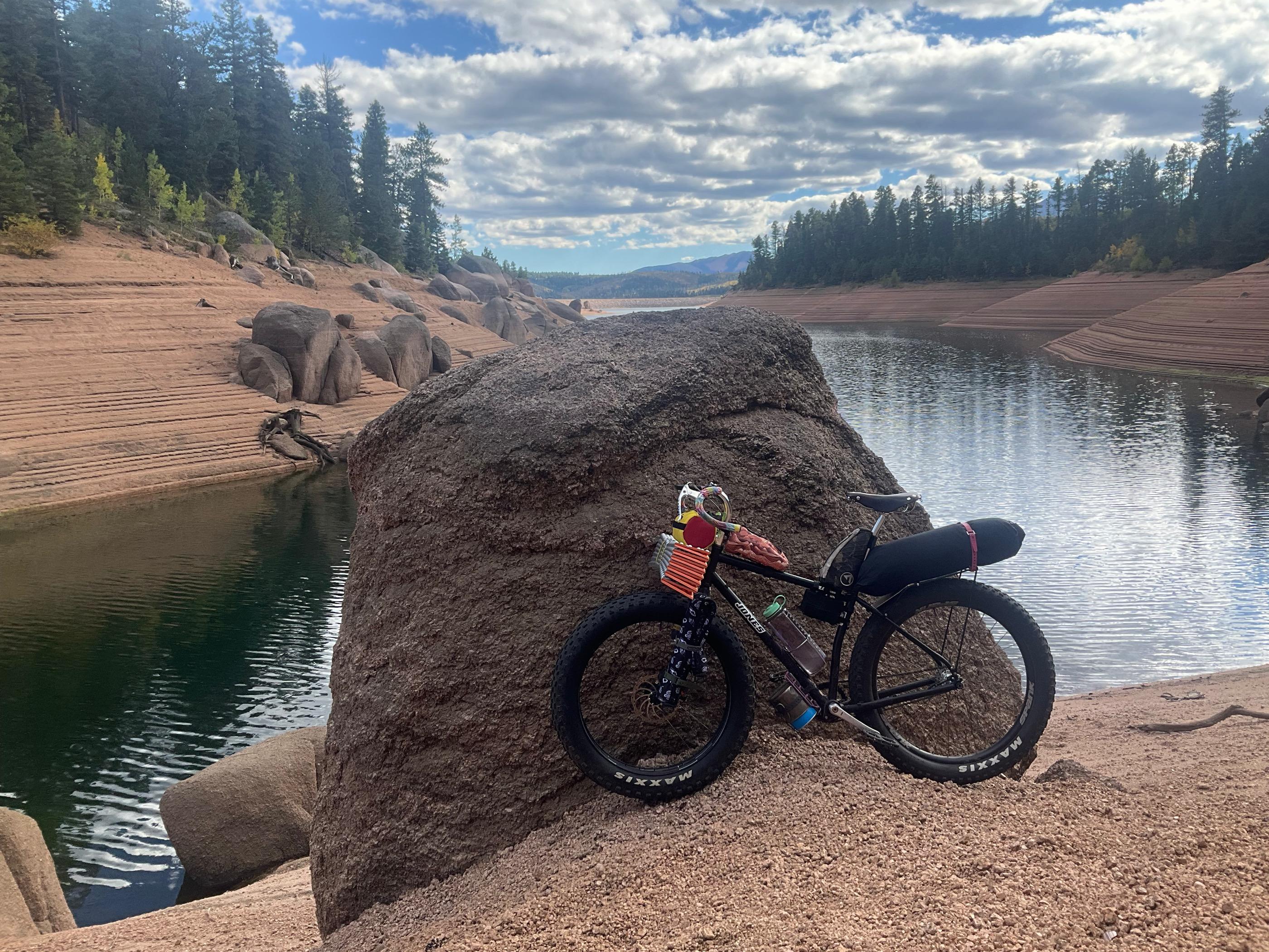 Fixie Dave's Jones fat bike leaned against a large granite boulder above the reservoir's rocky shoreline, cloudy sky overhead