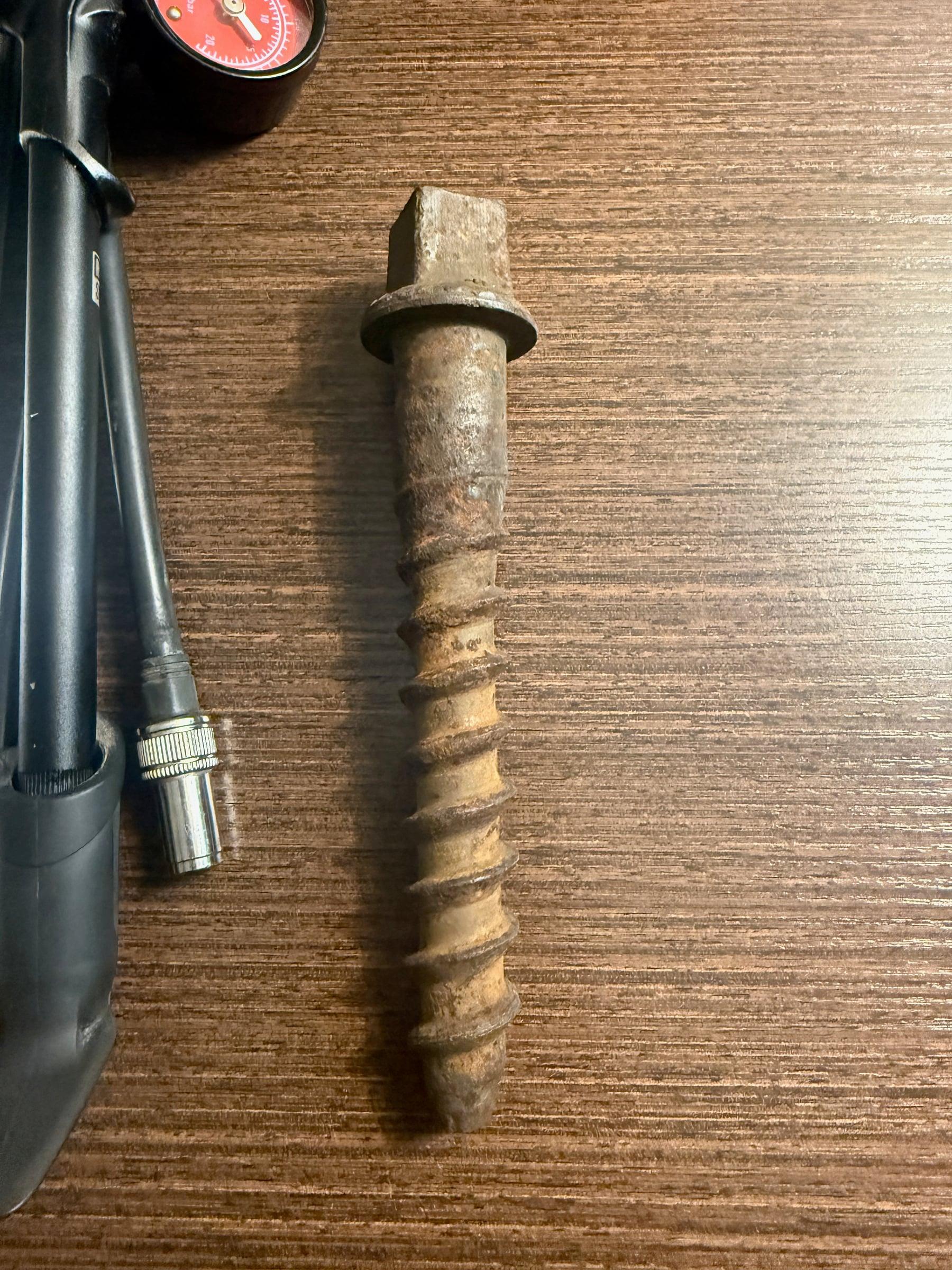 A rusty railroad spike lying on a wooden table next to a black shock pump