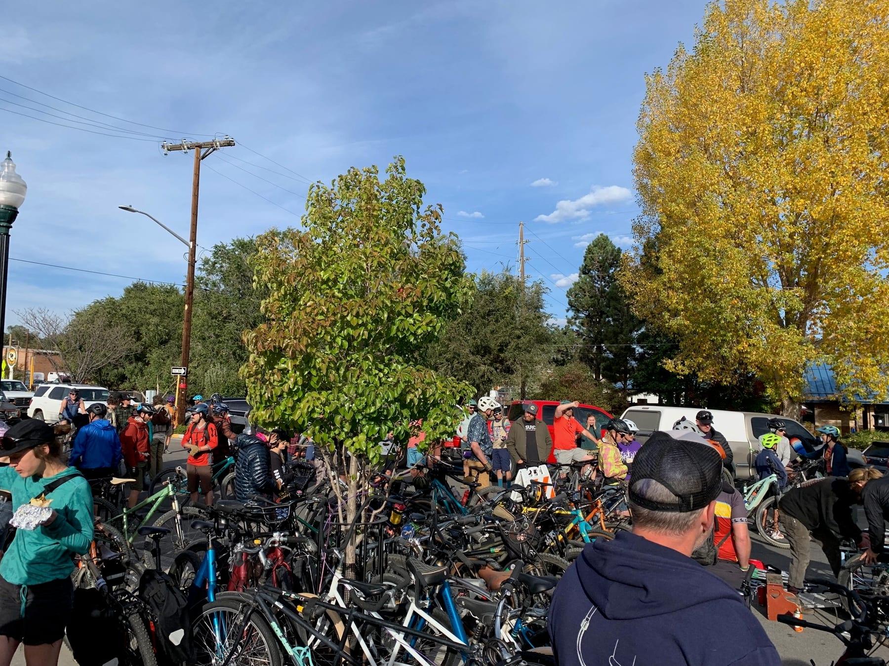 Large group of riders and bikes gathered outdoors with fall colors in the background