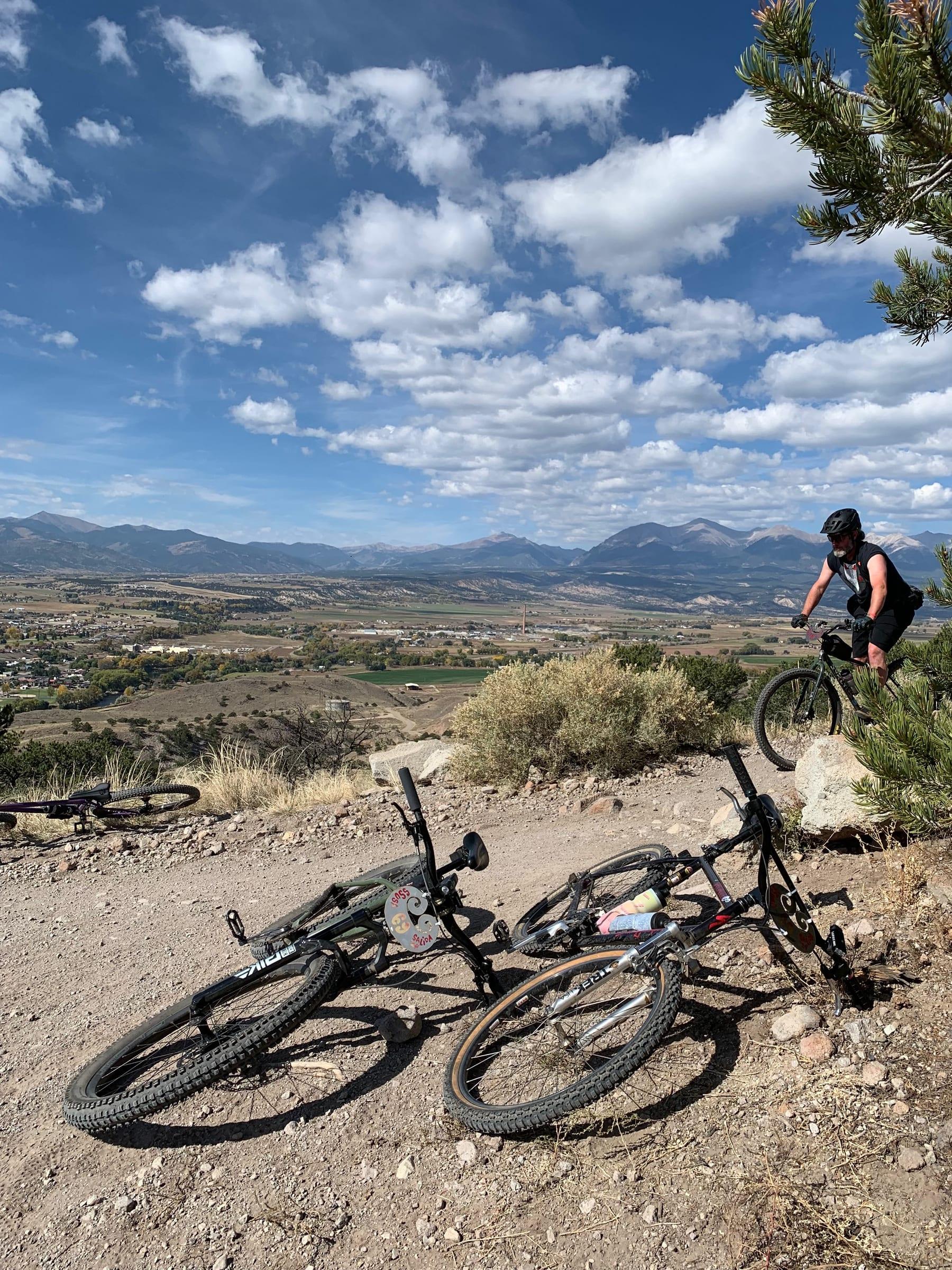 Rider looking out over the Salida valley from the trail, two bikes dropped in the foreground