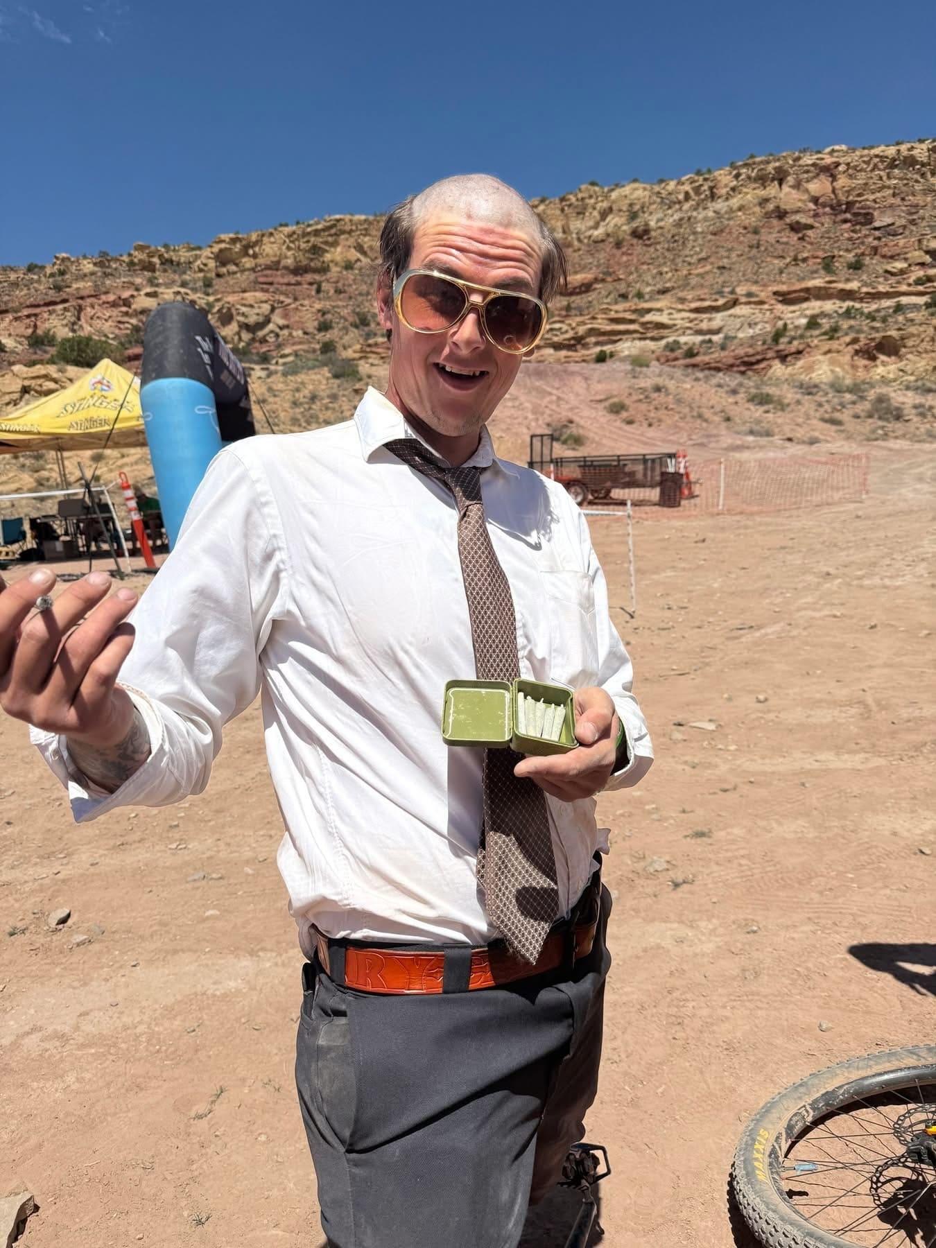 Rider in a dress shirt and tie holding a lighter and a beer in the desert parking area