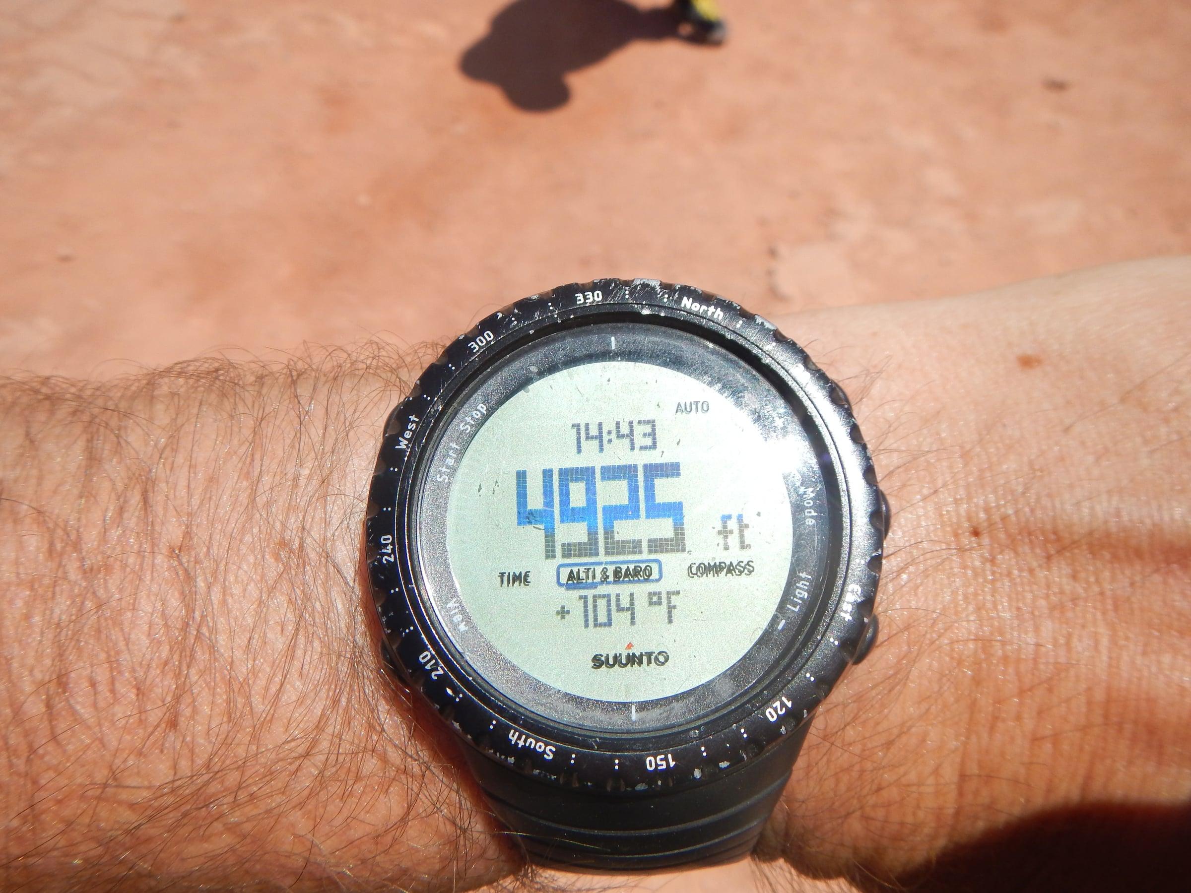 A worn, dusty Suunto Core on the wrist in the desert, showing altitude and temperature
