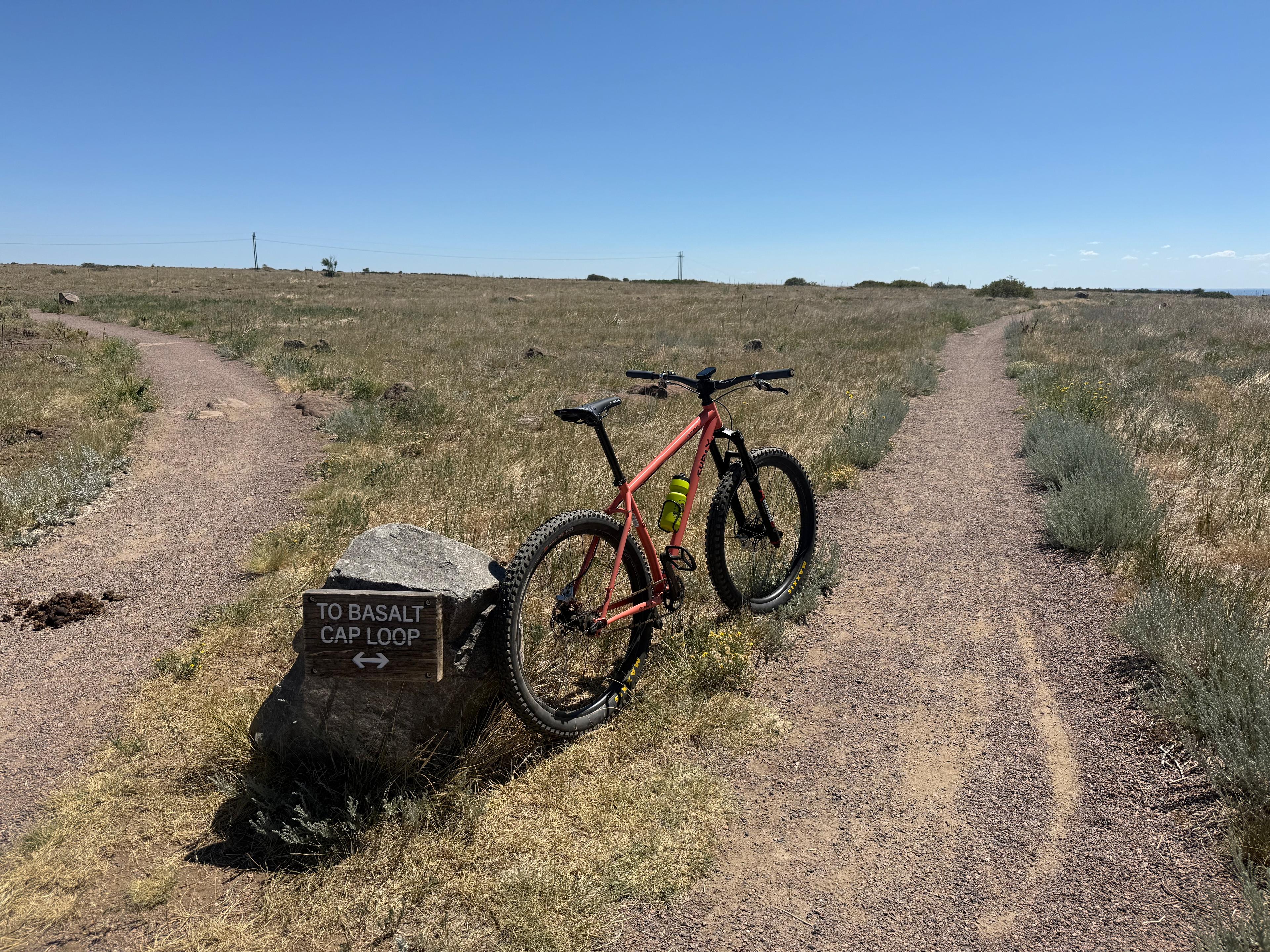 Trail marker reading TO BASALT CAP LOOP at the top of the climb, with a single-speed mountain bike leaning against the sign post