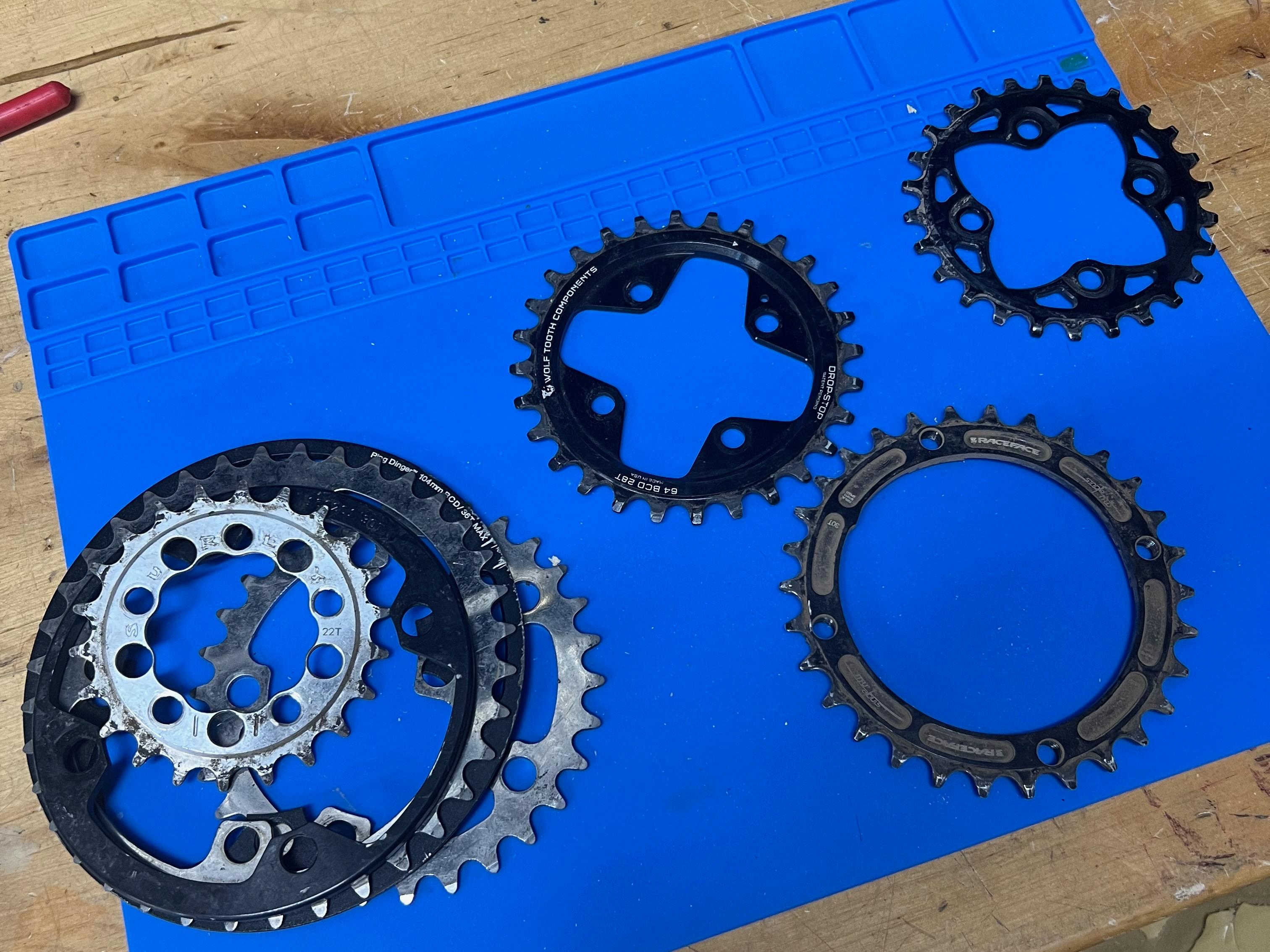 An assortment of chainrings with different tooth counts laid out on a workbench mat