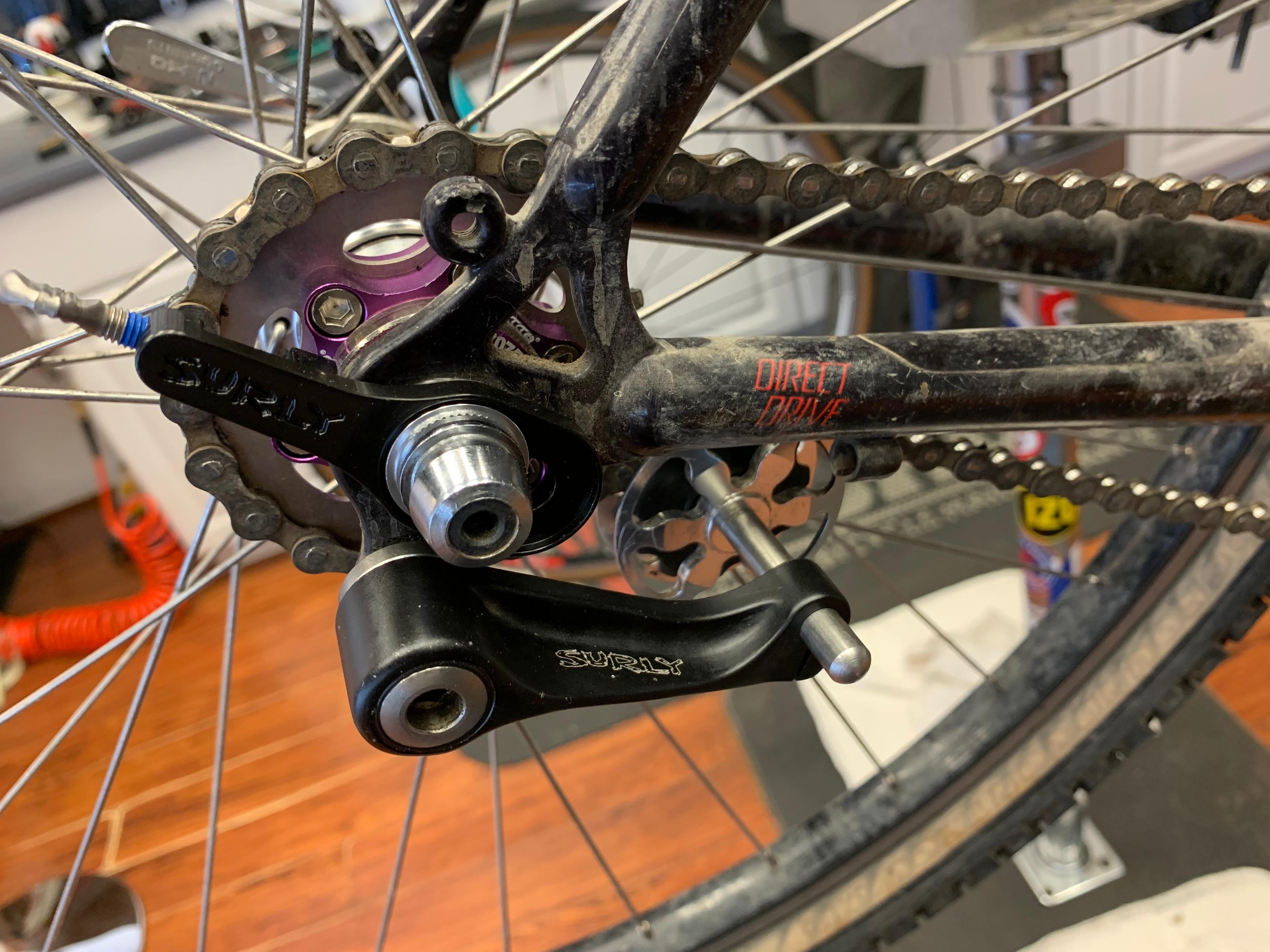 Close-up of a single-speed conversion on vertical dropouts, showing a Surly chain tensioner and axle hardware holding the rear wheel in place